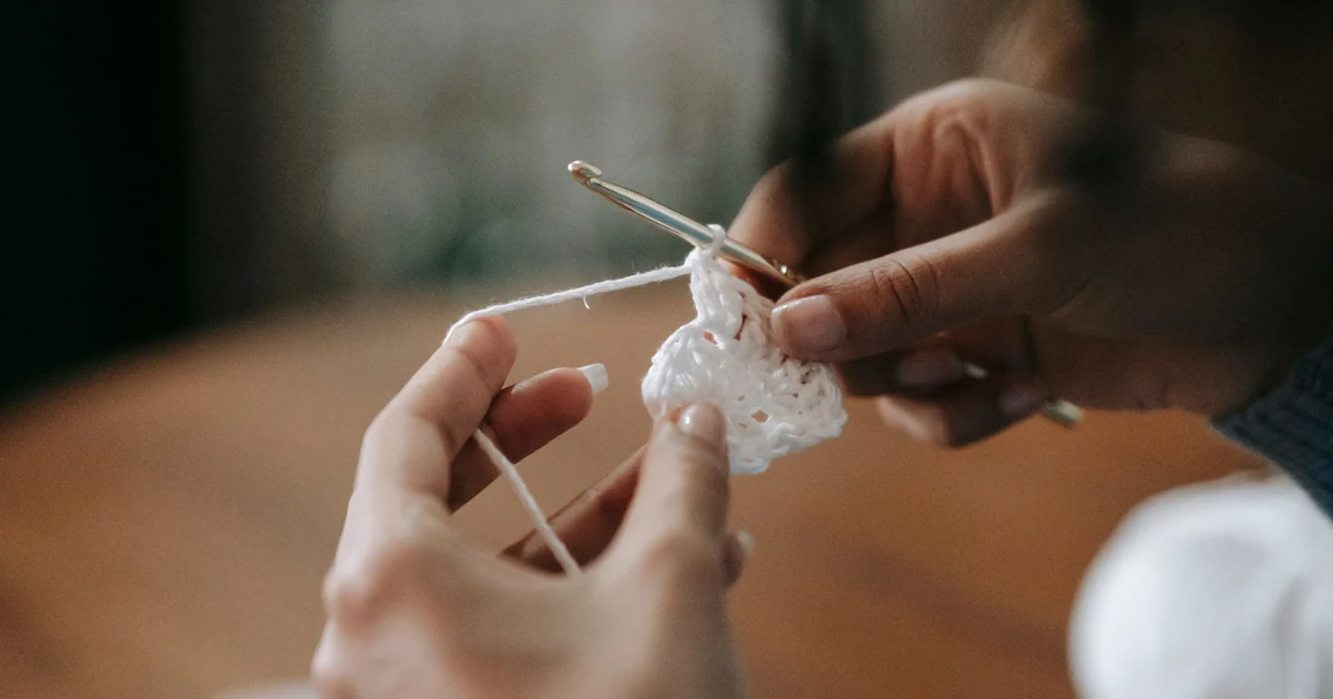 Hands holding crochet tools beside a small sample.