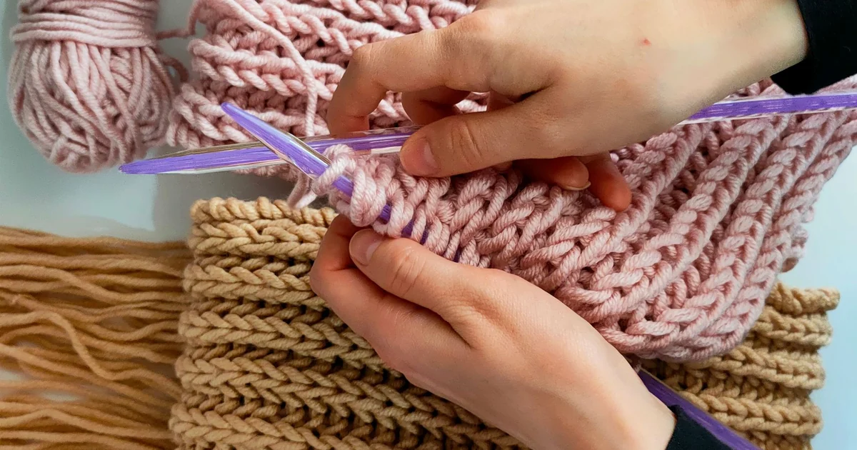 Close-up of hands crocheting a pink and cream scarf.