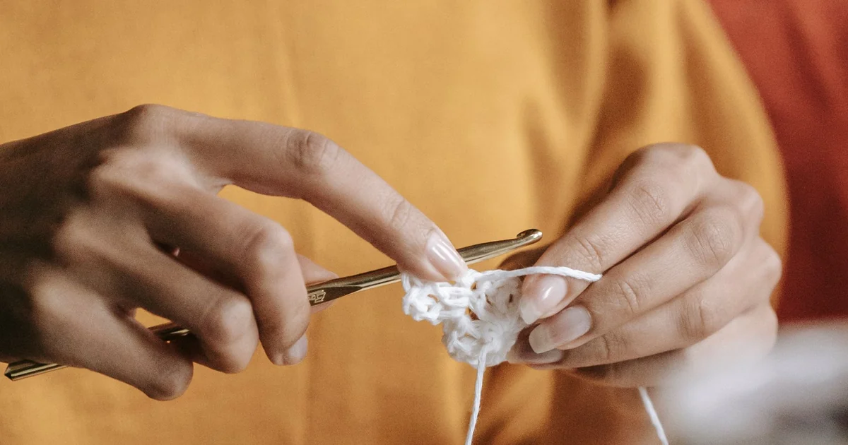 Hands crocheting a small white round piece with a hook.