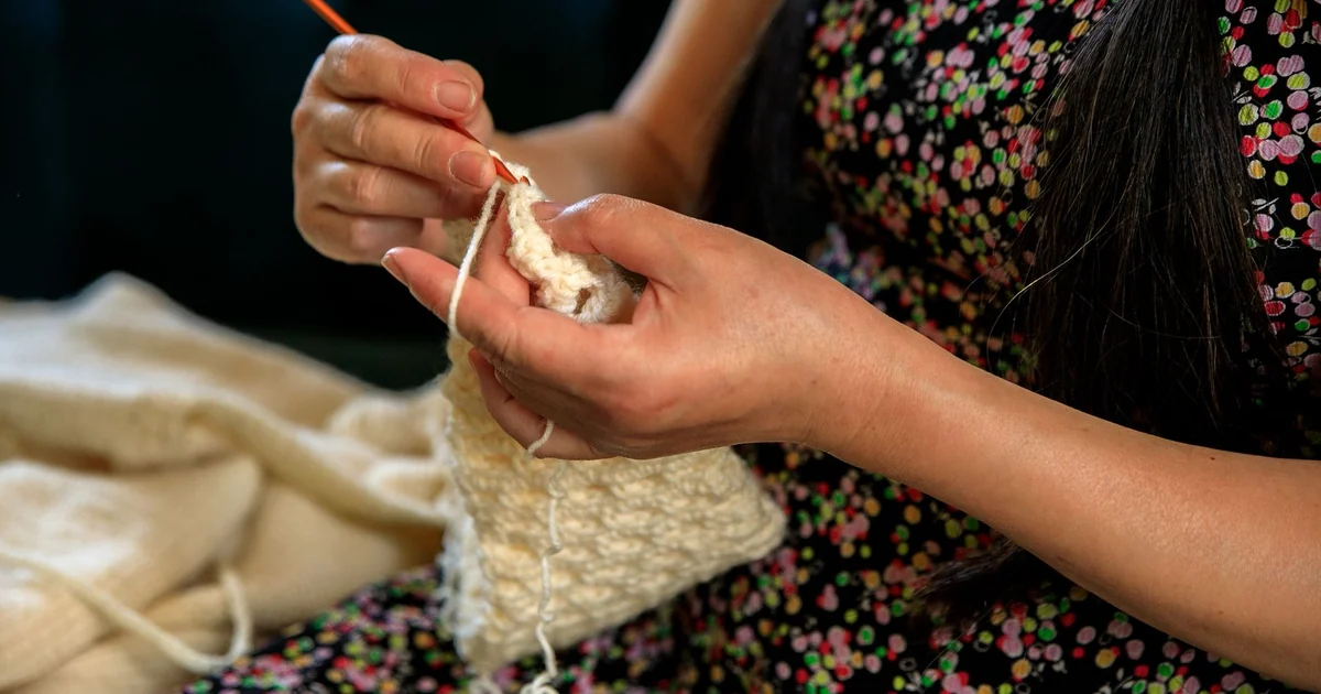 Hands holding a crochet square while working a corner.