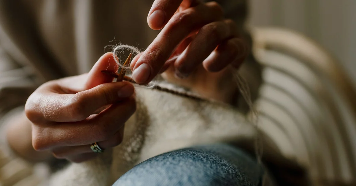 Hands working a neutral crochet blanket with a hook.