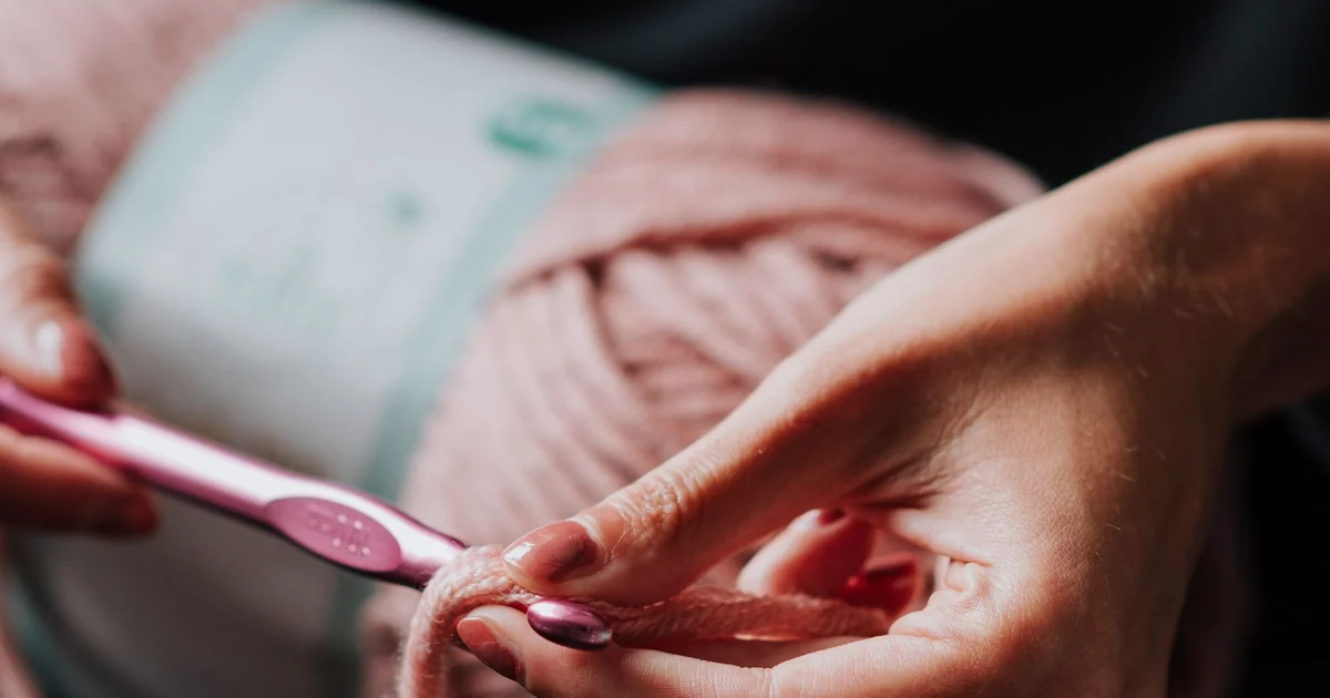 Close-up of hands using a pink crochet hook while changing yarn color.