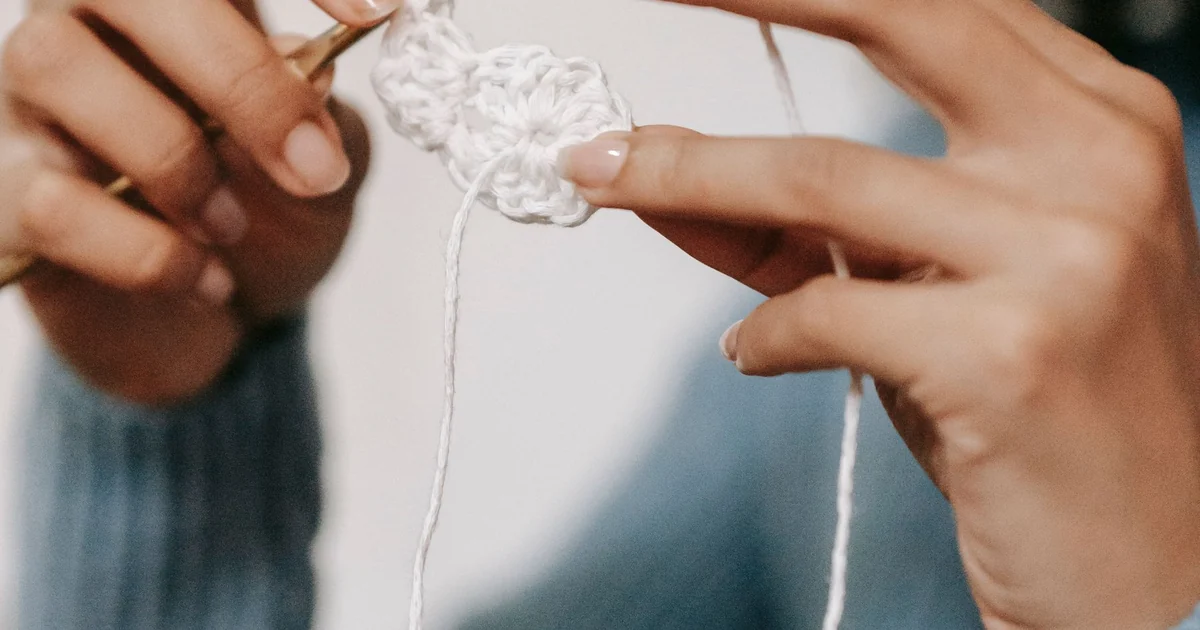 Hands working light blue yarn into a small crochet swatch.