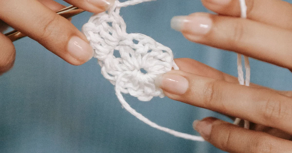 Hands holding a white crochet swatch with its stitches visible.