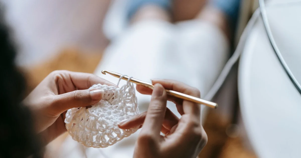 Hands using a metal hook to finish a white crochet sample.