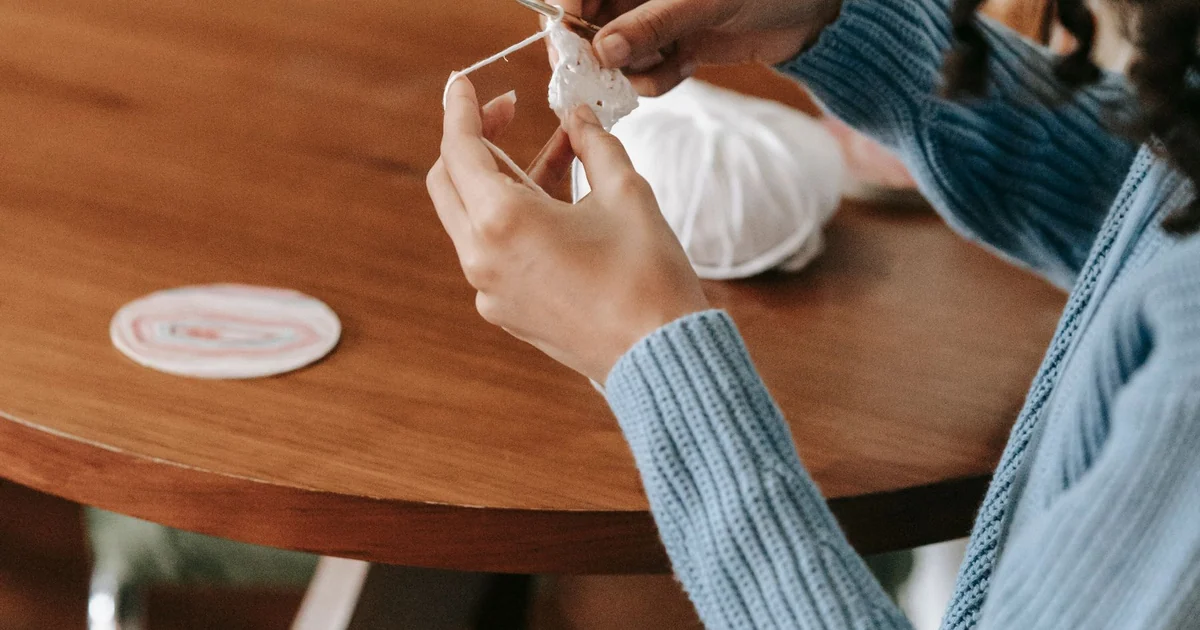 Person crocheting at a table with a small project.