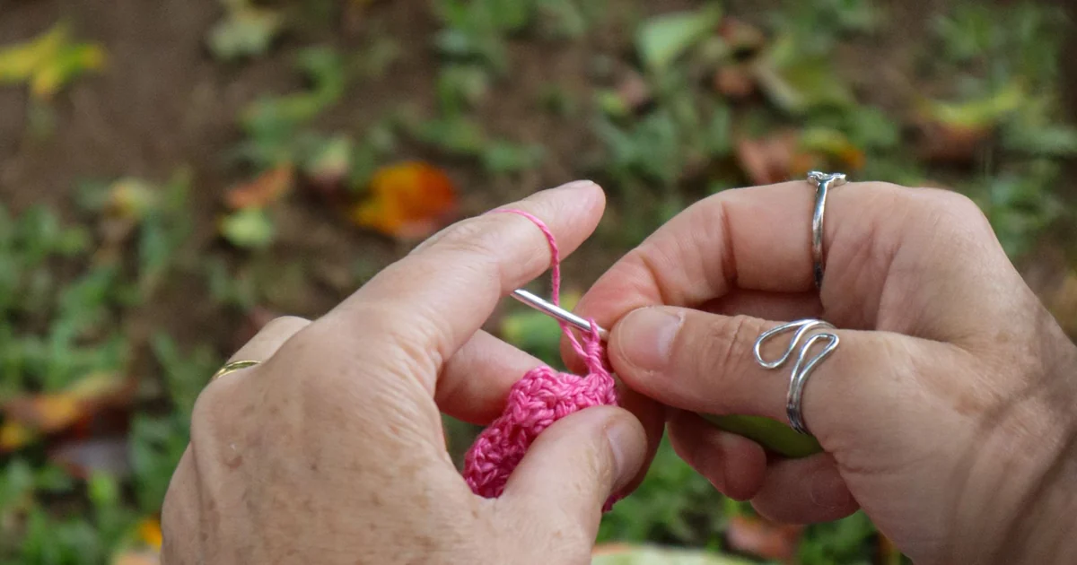 Hands making pink crochet stitches with a hook.