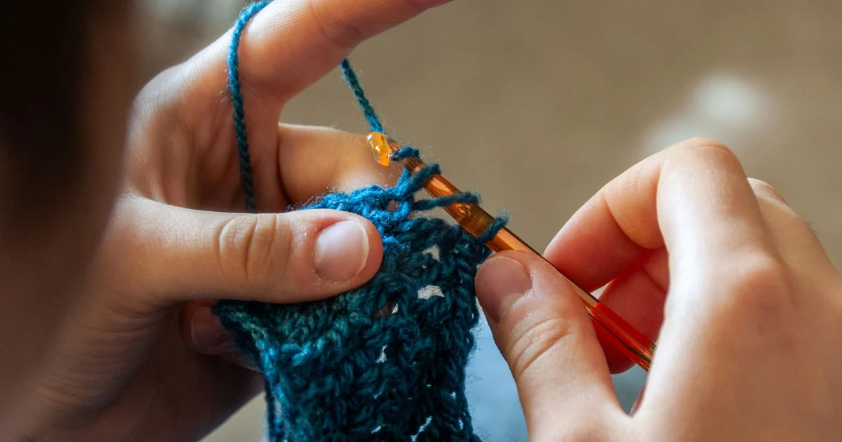 Hands crocheting dark blue fabric with a tan hook.