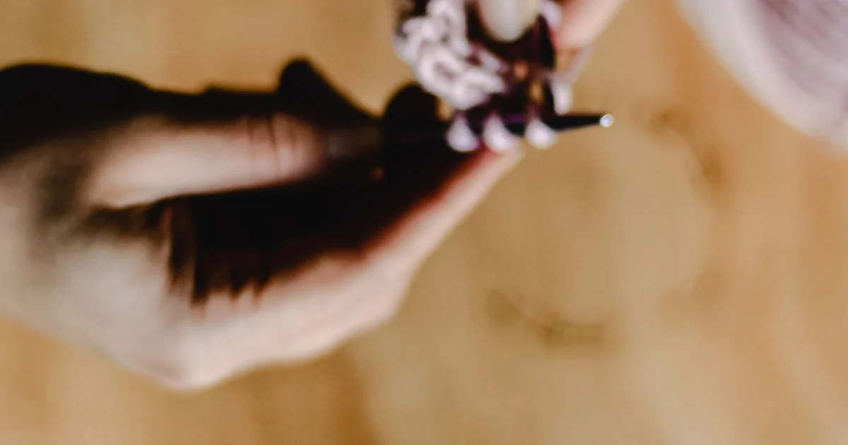 Close-up of fingers, a crochet hook, and white yarn against a dark background.