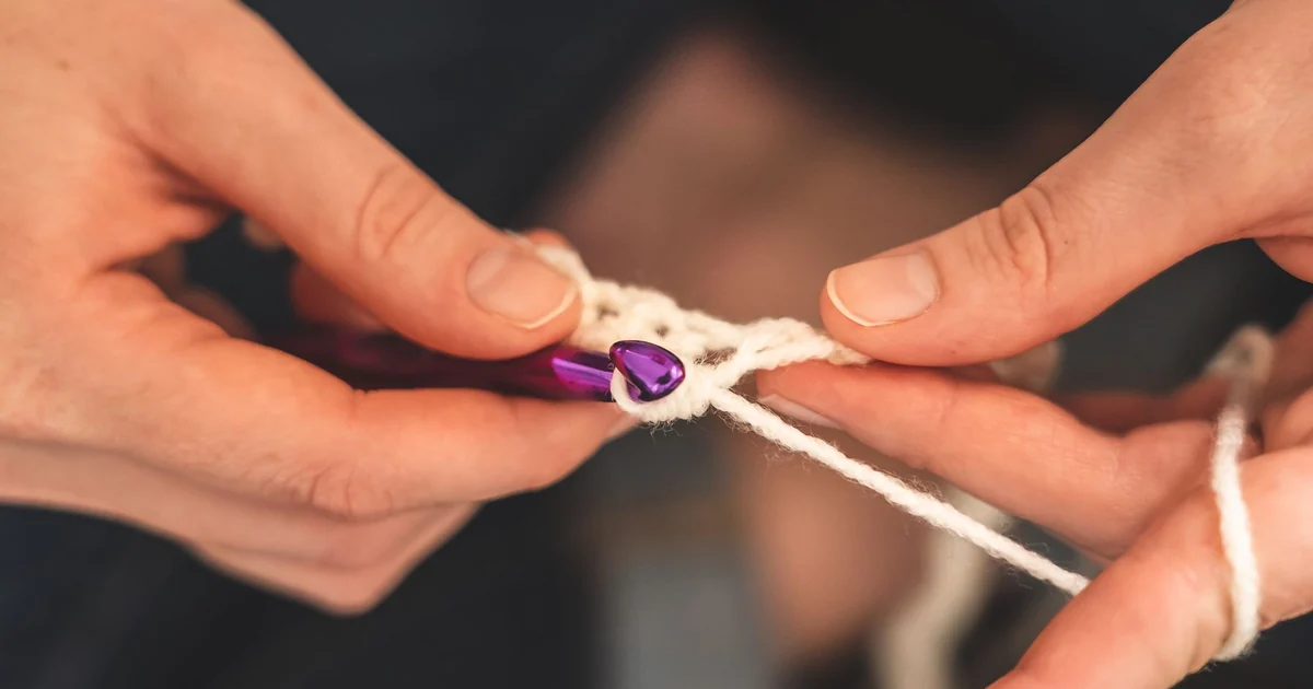 Close-up of a purple hook drawing white yarn through crochet loops.