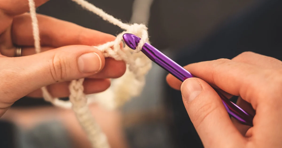 Hands holding a crochet row beside a purple crochet hook.