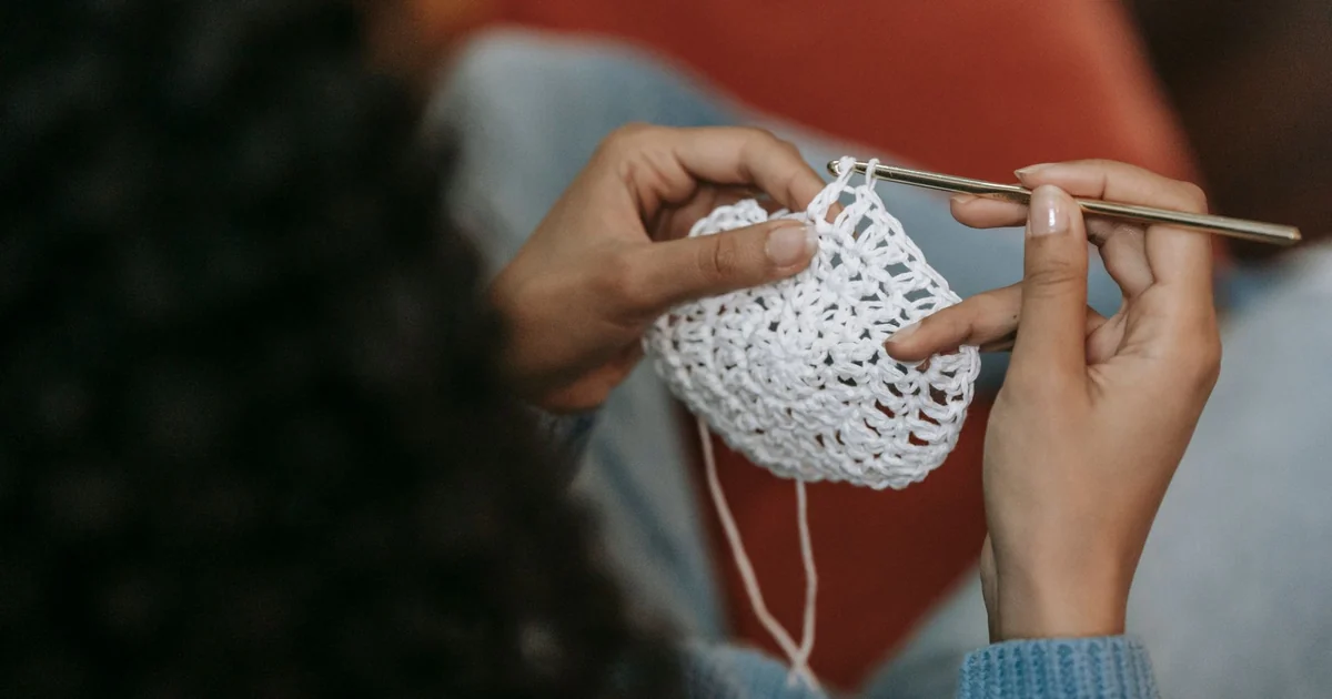 Hands weaving a yarn tail into the back of white crochet stitches.
