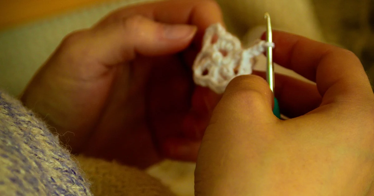 Close-up of a hand crocheting a small sample with a hook.
