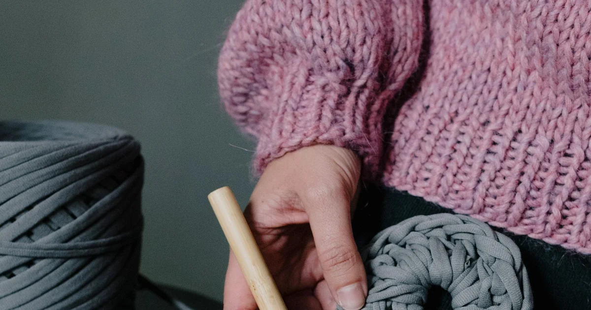 Hands holding a crochet fabric beside a crochet hook for measuring.