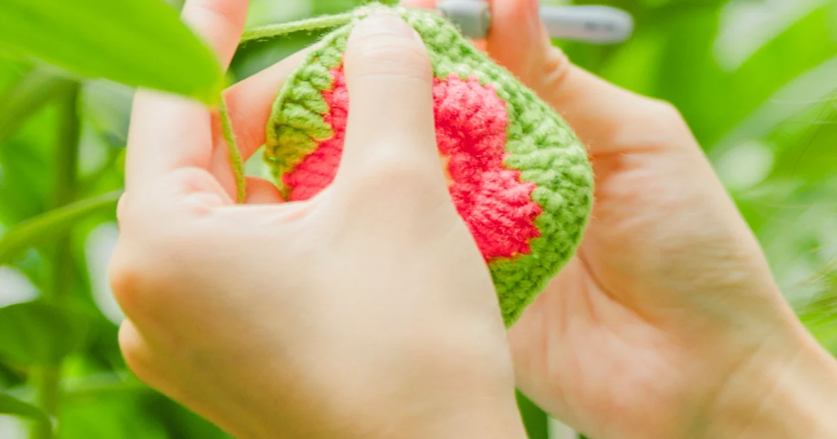 Hands holding a small green and pink crochet motif.
